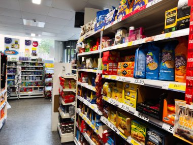 Manchester, İngiltere - 26 Eylül 2025: Küçük bir Tesco dükkanında raflarda yiyecek poşetleri, kutular ve fiyat etiketlerini gösteren parlak koridor.