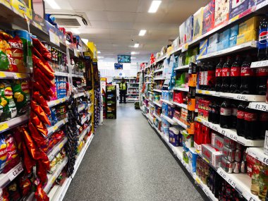 Manchester, İngiltere - 26 Eylül 2025: Kalabalık bir Tesco süpermarket koridorunda içi cips ve gazoz dolu parlak rafların arasında alışveriş yapan kişi.