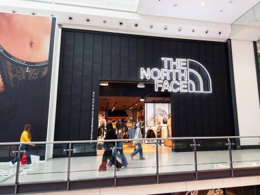 Manchester, İngiltere - 26 Eylül 2025: Müşteriler şık bir Kuzey Yüzü perakende alanına cesur neon logosuyla ve parlak siyah cepheleriyle girerler.