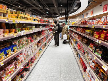 Manchester, İngiltere - 26 Eylül 2025: İyi stoklanmış bir Oseyo marketinde müşteriler yoğun bir alışveriş gezisi sırasında çeşitli Asya erişte bardakları ve atıştırmalıkları keşfediyorlar.