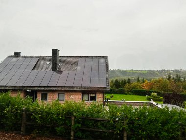 Liege, Belçika - 20 Ekim 2023: Belçika 'da güneş panelleri ve tarlalarla çevrili yeşil bir bahçeli konforlu tuğla ev.