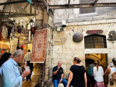 Kudüs, İsrail - 16 Eylül 2023 Kudüs, İsrail 'deki taştan kemerlerin altında müşteriler, satıcılar ve renkli tekstil ürünleriyle dolu hareketli bir kasaba manzarası. Via Dolorosa, Statio VII