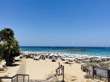 Paralimni, Kıbrıs - 18 Temmuz 2024: Güneşli bir günde Paralimni Kıbrıs Protaras Sahili, şemsiyeli, güneşli ve berrak mavi su.