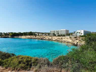 Paralimni, Kıbrıs - 18 Temmuz 2024: Paralimni Kıbrıs 'ta turkuaz su, kayalık kıyı şeridi ve modern Sunrise Jade otel binaları yer alıyor.