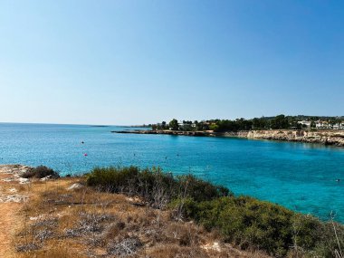 Paralimni, Kıbrıs - 18 Temmuz 2024: Paralimni Kıbrıs 'ta turkuaz deniz, kayalık sahil ve kıyı bitkilerini gösteren sakin bir Akdeniz Koyu.