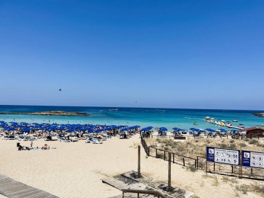 Paralimni, Kıbrıs - 18 Temmuz 2024: Kıbrıs Rum Kesimi 'nin Paralimni kentinde mavi şemsiyeli, güneşli ve berrak turkuaz su.