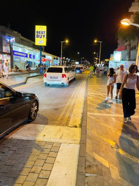 Paralimni, Kıbrıs - 18 Temmuz 2024: Paralimni Kıbrıs 'ta yayalar, arabalar ve parlak mağazaların yer aldığı canlı bir gece sokağı.