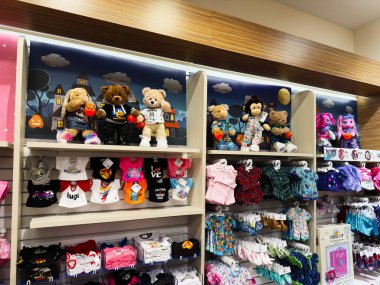 Manchester, İngiltere - 26 Eylül 2025: Renkli çocuk kıyafetleri ve peluş ayılar parlak kıyafetler ve neşeli Cadılar Bayramı balkabaklarıyla dükkan vitrinine hakim.