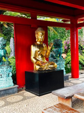 Madeira Portekiz 'in yemyeşil bahçesinde kırmızı bir pavyonda altın Buda heykeli, huzur ve dekoratif.