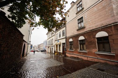 Tarnow, Polonya 'da ıslak bir sokak sahnesi, eski mimariyi, şemsiyeleri ve kasvetli bir sonbahar atmosferini gösteriyor..