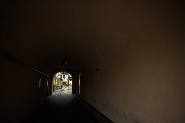 Tarnow, Polonya - 10 Ekim 2025: Karanlık tünel açık bir ara sokağa çıkıyor, kafeteryada oturma düzeniyle, dışarıda zıtlık ve gizem yaratıyor..