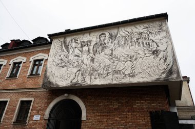 Tarnow, Polonya - 10 Ekim 2025: Tarnow, Polonya 'da bir tuğla cephesinde tek renkli kilise duvar resmi, birçok figürle dramatik bir dini sahneyi canlandırıyor..