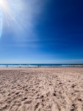 Nazik dalgalar ve uzak siluetlerle berrak gökyüzünün altında kıyı gününün tadını çıkaran parlak Lizbon sahili..