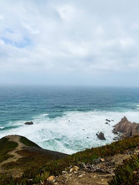 Kıyıda okyanus manzarası Bulutlu gökyüzünün altında engebeli kayalar ve dalgalar