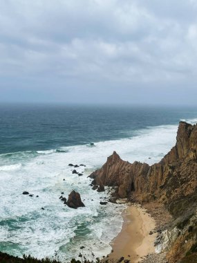 Dalgaların kumlu bir körfeze çarptığı engebeli uçurumlar boyunca dramatik sahil manzarası.