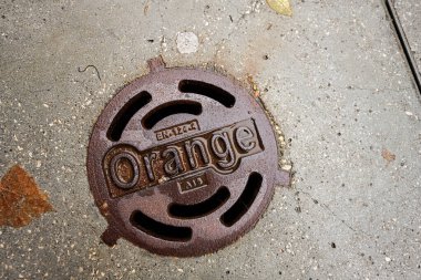 Tarnow, Polonya - 10 Ekim 2025: Paslı yuvarlak drenaj kapağı, beton kaldırımda turuncu renkle kaplı, kumlu bir şehir ortamında.