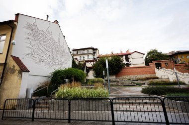 Tarnow, Polonya - 10 Ekim 2025: Şehrin ufuk çizgisi temalı bir Tarnow duvar resmi, tuğla duvarlar, merdivenler ve yeşillikler üzerine kurulu.