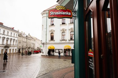 Tarnow, Polonya - 10 Ekim 2025: Polonya 'da Tarnow Caddesi' nde Strusinianka tabelası ve yayalarla dolu ıslak kaldırım taşları.