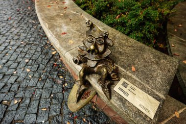 Tarnow, Polonya - 10 Ekim 2025: Bronz Maszkaron Trefni Goblin heykeli Tarnow, Polonya 'da yıpranmış bir plaketin yanındaki kaya tünemişti..