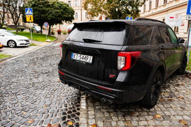 Tarnow, Polonya - 10 Ekim 2025: Yağmurdan sonra Polonya 'nın Tarnow kentinde ıslak bir kaldırım taşı caddesinde park etmiş koyu renkli bir Ford Explorer ST SUV.