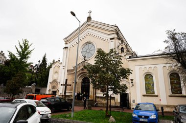 Tarnow, Polonya - 10 Ekim 2025: Tarnow, Polonya 'daki Kutsal Haç ve Azizler Kilisesi cephesi park halindeki araba ve ağaçların yanında bir şehir caddesinde.