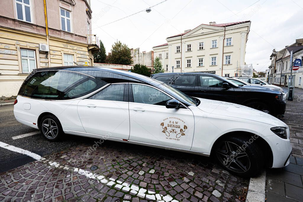 Tarnow, Poland - October 10, 2025: Elegant white Mercedes Benz hearse parked on cobblestones in Tarnow, Poland, showcasing a classic crest emblem on the door.