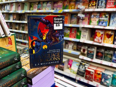 Manchester, İngiltere - 26 Eylül 2025: S. F. Williamson 'un yazdığı Ejderhalar Dili adlı kapak, yoğun bir kitapçıda ejderha sanat eserlerinin sergilendiği canlı bir mavi kapağa sahip..