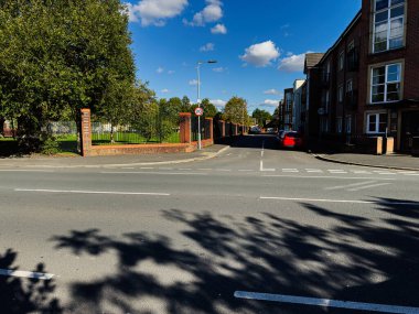 Manchester 'da duvarları tuğlalı, kırmızı arabası ve yapraklı ağaçları olan güneşli bir sokak manzarası..
