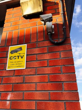 Manchester, İngiltere 'de bir tuğla binanın güvenlik kamerası yanında sarı CCTV tabelası..
