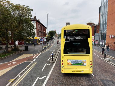 Manchester, İngiltere - 29 Eylül 2025: Manchester 'da işlek bir yolda, dükkan ve bisikletçilerin yanında parlak sarı bir çift katlı otobüs.