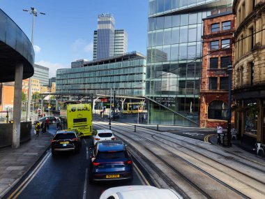 Manchester, İngiltere - 29 Eylül 2025: Manchester 'da tramvay rayları, modern cam kooperatif sigorta derneği mimarisi ve araçları içeren hareketli kentsel sahne.