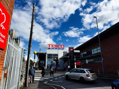 Manchester, İngiltere - 29 Eylül 2025: Tesco yakınlarındaki Manchester Caddesi 'nde müşteriler, arabalar ve modern alışveriş merkezi dış girişi.