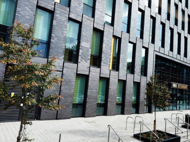 Manchester, İngiltere - 29 Eylül 2025: Manchester 'da bir şehir caddesi boyunca uzun pencereler ve bir restoran vitrininin bulunduğu çağdaş tuğla dış görünüş. 1853 Manchester Koleji Restoranı