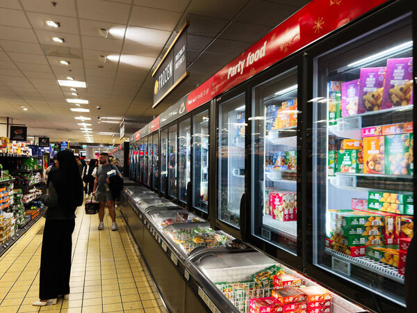 Manchester, UK - September 29, 2025: Shoppers browse frozen foods in a long supermarket aisle in Manchester, UK.