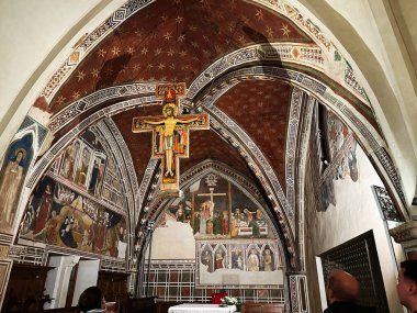 Assisi, İtalya - 16 Ekim 2024: Assisi, İtalya 'nın içinde, tarihi bir kilise süslü freskler, yıldızlı kırmızı kemerler ve asılı bir haç bulunmaktadır..