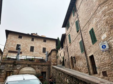 Assisi, İtalya - 16 Ekim 2024: Taş binalar, dar sokaklar ve açık teras kafelerin yer aldığı büyüleyici Assisi sahnesi.