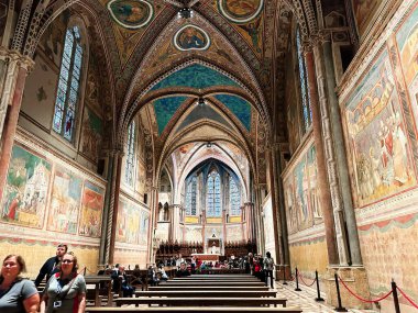 Assisi, İtalya - 16 Ekim 2024: Ziyaretçiler zengin dekore edilmiş bir ortaçağ kilisesinin ahşap sıralarında oturuyorlar..