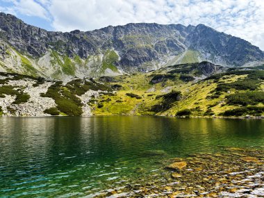 Kristal berrak göl, çimenli yamaçlar Zakopane yakınlarındaki kayalık zirvelere çıkarken engebeli tepeleri yansıtır..