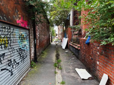 Manchester, İngiltere - 30 Eylül 2025: Tuğla duvarları, grafitileri, bitkileri ve atılmış döküntüleri olan Manchester kentsel sokağı.