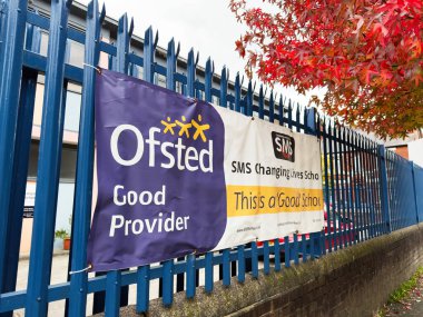 Manchester, İngiltere - 30 Eylül 2025: Sonbahar yaprakları Manchester SMS Değişen Yaşamlar Okulu 'nun önünde iyi hizmet veren afişlerle birlikte mavi bir çit oluşturuyor.