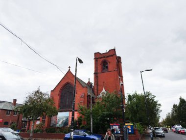 Manchester, İngiltere - 30 Eylül 2025: Manchester 'da bulutlu bir günde kırmızı tuğlalı St John' s Centre Kilisesi, uzun bir kulesi, arabaları, ağaçları ve işlek bir sokak.