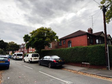 Manchester, İngiltere - 30 Eylül 2025: Manchester, İngiltere 'deki Residential Leighton Rd sokak sahnesi kırmızı tuğlalı evler, çit duvar ve sessiz bir cadde boyunca park edilmiş arabalar.
