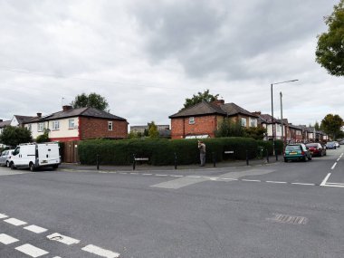 Manchester, İngiltere - 30 Eylül 2025: Tuğladan evler, uzun bir çit ve bulutlu bir günde park edilmiş arabalarla sakin bir Manchester caddesi.