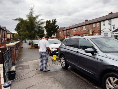 Manchester, İngiltere - 30 Eylül 2025: Bir adam Manchester 'da bir yerleşim yerindeki gri bir SUV' yi elektrikli çamaşır makinesiyle temizliyor.