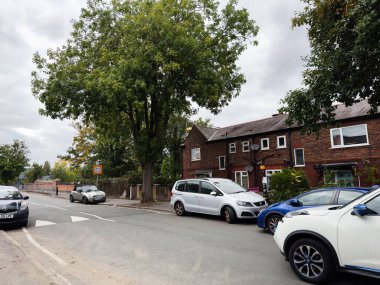 Manchester, İngiltere - 30 Eylül 2025: Manchester 'da sakin kentsel sokak sahnesi tuğla evler, park edilmiş arabalar ve uzun bir ağaç.