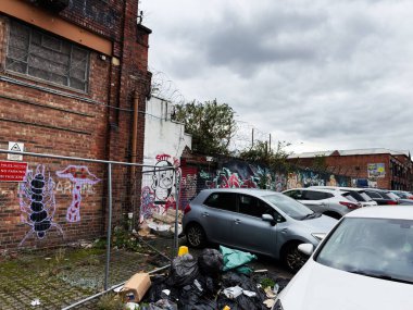 Manchester, İngiltere - 30 Eylül 2025: Manchester 'da duvar yazıları, park edilmiş arabalar ve bir yığın çöp içeren şehir sahnesi.