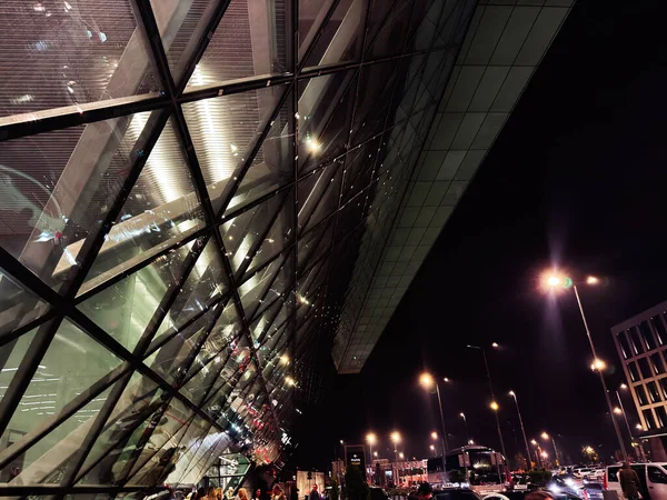 Balice, Polonya - Ekim 04, 2025: Krakow, Polonya 'da gece yarısı modern cam bina, aydınlanmış sokaklar ve trafik kentsel atmosfer yaratıyor. Krakw John Paul II Uluslararası Havaalanı