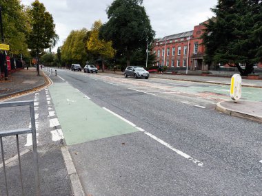 Manchester, İngiltere - 30 Eylül 2025: Sonbaharda yeşil bisiklet şeridi, arabalar ve kırmızı tuğlalı bir binası olan Manchester City Caddesi.