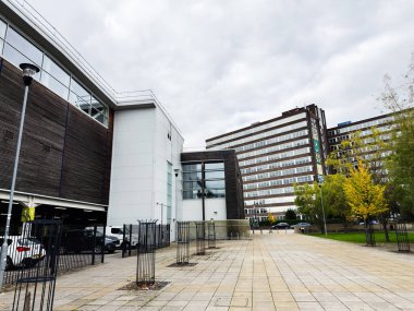 Manchester, İngiltere - 30 Eylül 2025: Manchester, İngiltere 'de cam binalar, geniş bir plaza ve park halindeki arabaların yer aldığı çağdaş iş bölgesi sahnesi.