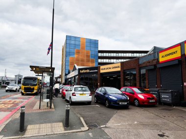 Manchester, İngiltere - 30 Eylül 2025: Araçlar Manchester, İngiltere 'de modern bir fayans binası ve otomobil hizmetlerinin yanında işlek bir cadde üzerindedir.